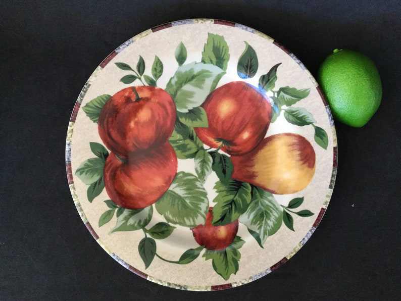 May include: A white ceramic dinner plate with a brown rim and a colorful design of apples and pears on a vine. The plate has a rustic, farmhouse style.