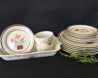 May include: A vintage dinnerware set featuring plates, bowls, and ramekins. The cream-colored pieces are adorned with a floral design in orange and brown, complemented by brown and peach-colored bands. A rectangular serving dish is also included.