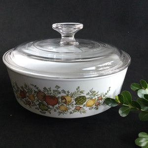 May include: White ceramic casserole dish with a clear glass lid. The dish features a floral design with green leaves and colourful vegetables.