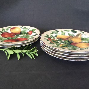 May include: Set of four white ceramic dinner plates with a fruit design. The plates feature a green leafy background with red apples and yellow pears.