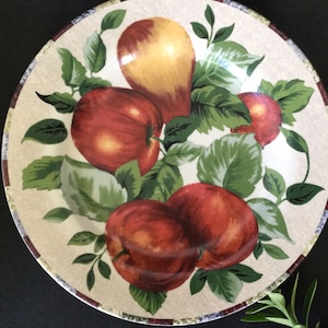 May include: A white ceramic dinner plate with a brown rim features a colorful design of red apples and a yellow pear with green leaves.