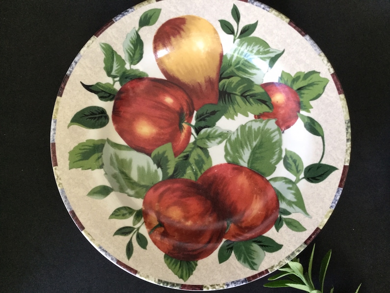 May include: A white ceramic dinner plate with a brown rim features a colorful design of red apples and a yellow pear with green leaves.
