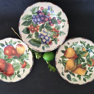 May include: Three ceramic plates with a white background and colorful fruit designs. The plates feature grapes, apples, and pears.