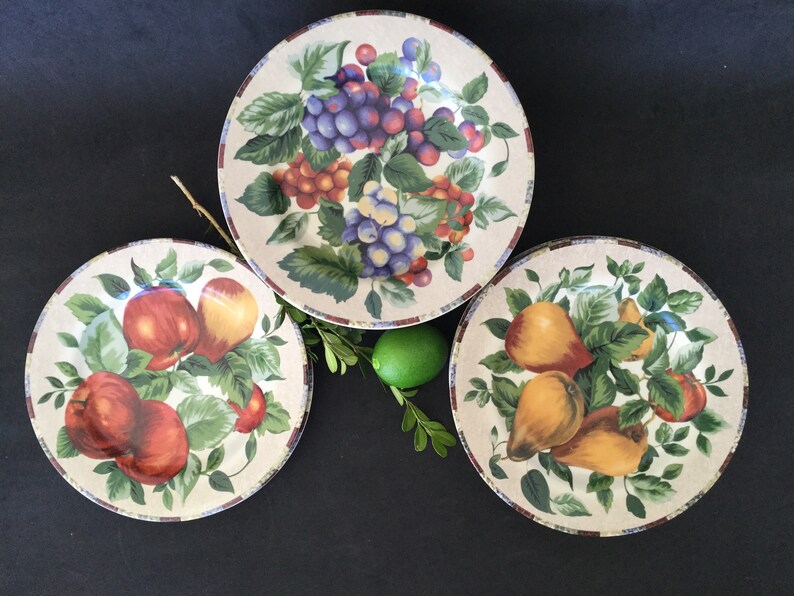 May include: Three ceramic plates with a white background and colorful fruit designs. The plates feature grapes, apples, and pears.