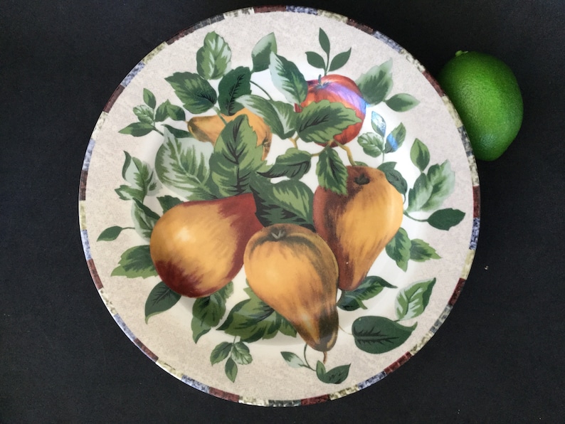 May include: A white ceramic plate with a brown rim features a colorful illustration of pears and apples on a green vine. The plate has a rustic, farmhouse style.