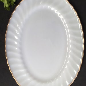 May include: White oval serving platter with a gold rim. The platter has a fluted design.