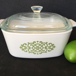 May include: White casserole dish with a clear glass lid and a green decorative design. The dish has a rectangular shape with rounded corners and handles. A green lime sits next to the dish.