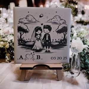 May include: A square, light grey tile featuring a black and white illustration of a bride and groom holding hands. The tile is displayed on a small wooden easel. The date "03 20 25" is printed on the tile.