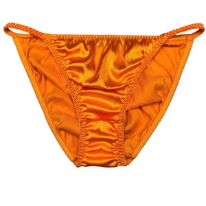May include: Bright orange satin underwear with a low-rise cut. The edges are trimmed with a matching color, and the waist and leg openings have a delicate, gathered detail. The fabric has a shiny, smooth texture.