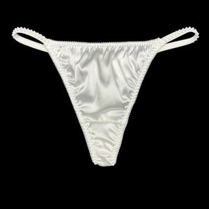 Könnte beinhalten: Elfenbeinfarbener String-Tanga aus seidig-glattem Stoff. Das Kleidungsstück hat zarte, gewellte Kanten und dünne Träger. Der Hintergrund ist einfarbig schwarz und hebt die Details der Dessous hervor.