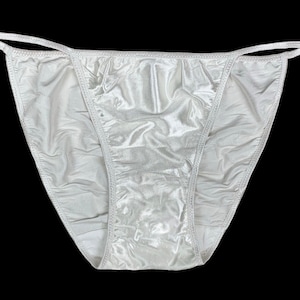 May include: White satin lingerie with a delicate lace trim. The garment has a low-cut back and a high-cut leg.