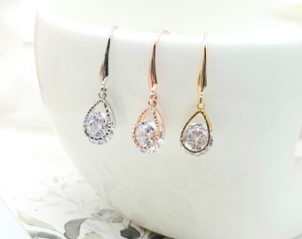 May include: Three drop earrings featuring a central round clear stone encased in a teardrop-shaped metal frame. The set includes one silver-tone, one rose gold-tone, and one gold-tone earring, each suspended from a matching curved hook wire.