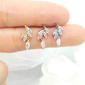 May include: Three dainty earrings with a leaf design featuring clear cubic zirconia stones. The earrings are available in gold, rose gold, and silver.