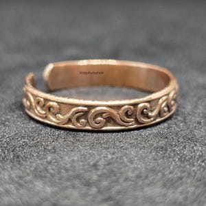 May include: A copper-colored adjustable ring with an ornate, swirling pattern. The ring's band features a detailed design of flowing lines and curls. The text "Visitpihufashion" is visible on the ring.