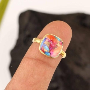 May include: A gold ring featuring a square turquoise gemstone. The gemstone displays a blend of pink, blue, and orange hues with gold flecks.