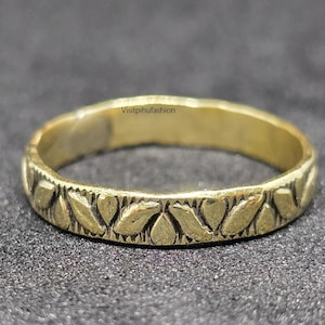 Könnte beinhalten: Ein goldfarbener Ring mit einem detaillierten Blattmuster um das Band. Der Ring ist vor einem dunklen Hintergrund platziert. Der Text "Visitpihufashion" ist auf dem Ring sichtbar.