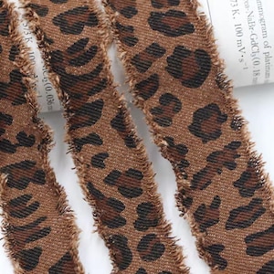 May include: Close-up of three strips of fabric with a brown leopard print pattern. The fabric has a frayed edge, and the leopard spots are dark brown on a lighter brown background. The fabric is likely used for crafting or sewing projects.