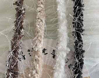 May include: Four strands of fuzzy trim in brown, beige, white, and black. The trim is braided and has a fluffy texture.