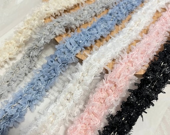 May include: Assortment of fluffy, textured trims in various colors, including white, gray, light blue, pink, black, and a shimmery gold thread running through each trim.