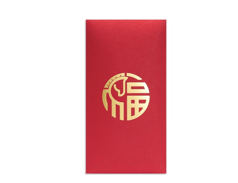 Puede incluir: Un sobre rojo con un dise&ntilde;o circular dorado que presenta un caballo estilizado y caracteres chinos. El sobre es rectangular y tiene una superficie lisa. El dise&ntilde;o est&aacute; centrado en la parte delantera.