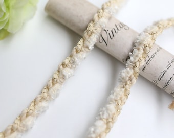May include: A close-up of a beige and gold trim with a fuzzy texture. The trim is wrapped around a rolled piece of paper with the word "Vintage" written on it.