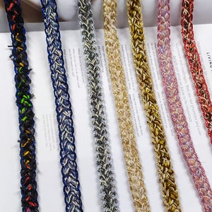 Puede incluir: Surtido de ribetes trenzados con acentos de purpurina en varios colores, incluidos negro, azul, plateado, dorado, beige, marrón y rosa. El ribete se muestra sobre una superficie blanca con texto.