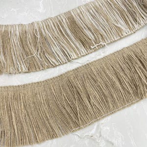 May include: Two pieces of brown and white fringe trim. The top piece has white fringe and the bottom piece has brown fringe.