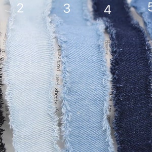 Puede incluir: Cinco cintas de denim de diferentes tonos de azul, azul claro y negro. Las cintas tienen un borde deshilachado.
