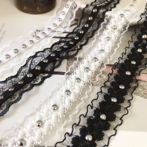 Könnte beinhalten: Drei verschiedene Spitzenborten mit silbernen Nieten. Die Borten sind schwarz, weiß und eine Kombination aus Schwarz und Weiß. Die Borten sind alle gekräuselt und haben einen zarten, femininen Look.