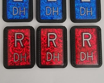 May include: Six rectangular, black-framed patches. Three have a blue glitter background with a white "L" and "DH". The other three have a red glitter background with a white "R" and "DH".