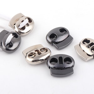 May include: Five toggle cord locks in different finishes: silver, black, and gunmetal. The cord locks are oval-shaped with two holes for threading cord.