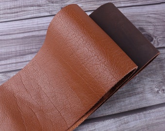 May include: Close-up of two pieces of leather. One is a rich, textured brown, and the other is a darker, chocolate brown. The leather is folded over, revealing the underside of the darker piece. The background is a light gray wooden surface.