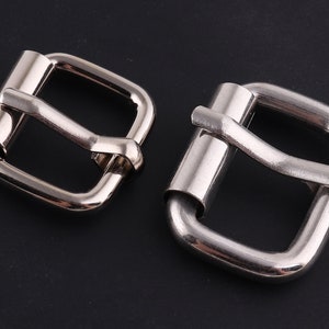 May include: Two shiny, silver-colored roller buckles. Each buckle has a rectangular frame with a central roller bar. The metal has a polished finish, reflecting light. These buckles are likely for belts or straps.
