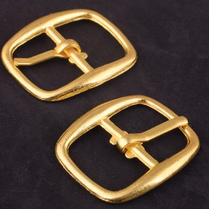 May include: Two gold metal belt buckles. The buckles are rectangular with a smooth, shiny finish. The buckles have a single prong.