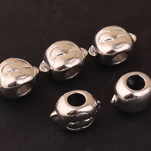 May include: Five silver metal beads with a face design. The beads have a hole in the centre for stringing.