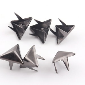Op de afbeelding: Een set van zes zilverkleurige metalen piramide studs met een puntige punt. De studs liggen in verschillende posities, sommige liggen plat en sommige staan rechtop.