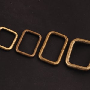 Op de afbeelding: Vier antieke goudkleurige metalen D-ringen in verschillende maten. De ringen zijn gerangschikt in een rij van de kleinste tot de grootste.