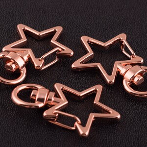 Puede incluir: Tres llaveros en forma de estrella de color oro rosa con cierres giratorios. Cada llavero tiene un tamaño y una forma diferentes.
