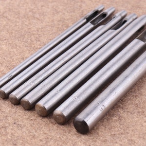 May include: Set of seven silver metal leather hole punches with different sizes, ranging from 2mm to 10mm. Each punch has a handle and a sharp tip.