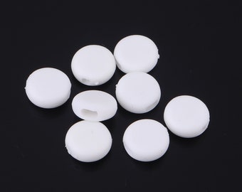 May include: Eight white plastic round beads with a hole in the center. The beads are arranged in a loose pile on a black surface.