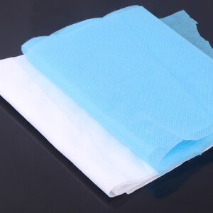May include: Two layers of non-woven fabric, one white and one light blue, folded together. The fabric is textured and appears to be soft.