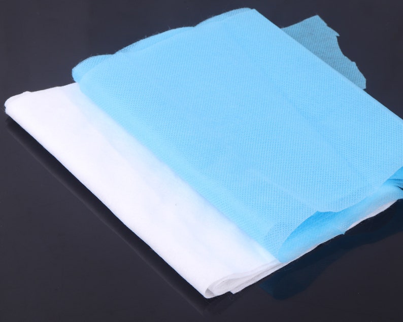 May include: Two layers of non-woven fabric, one white and one light blue, folded together. The fabric is textured and appears to be soft.