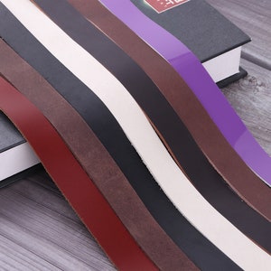 May include: Assortment of leather straps in various colours, including red, brown, black, white, and purple. The straps are arranged in a fan shape, with the purple strap at the top and the red strap at the bottom.