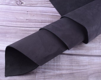 May include: A roll of black leather, folded and displayed on a wooden surface. The leather has a smooth, textured finish.