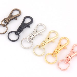 Pode incluir: Seis chaveiros de metal de diferentes cores com um fecho giratório e um anel. Os chaveiros são de cor ouro, prata, preto, bronze, ouro rosa e cobre.