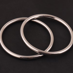 May include: Two silver metal hoops, one slightly larger than the other, are interlocked. The hoops are smooth and shiny.
