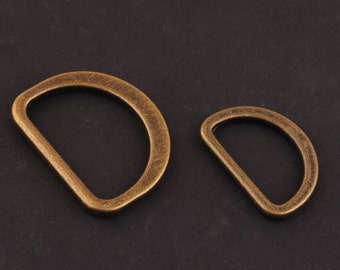 May include: Two antique gold-toned metal D-rings. The larger ring is about 2 inches in diameter and the smaller ring is about 1 inch in diameter.