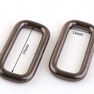 May include: Two black metal D-rings, one measuring 39mm in length and 14mm in width.