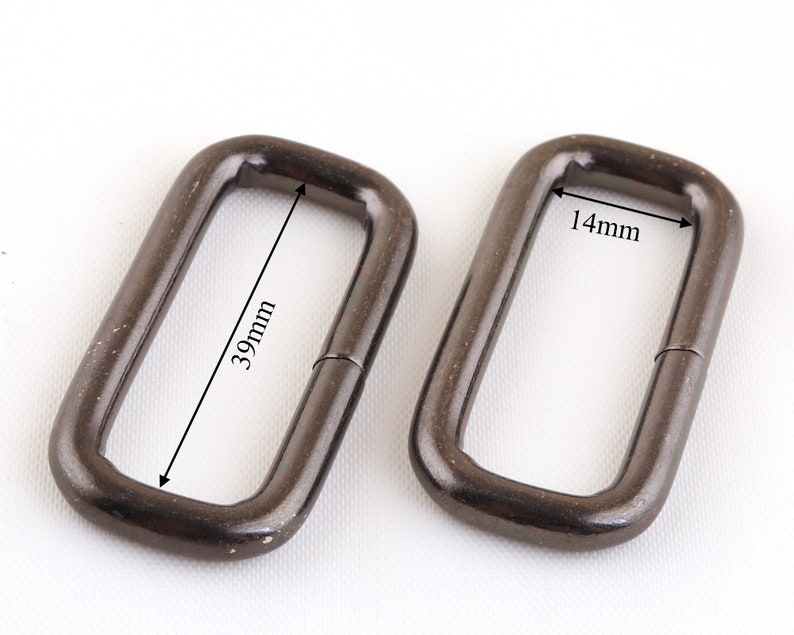May include: Two black metal D-rings, one measuring 39mm in length and 14mm in width.