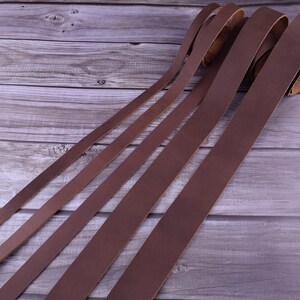 May include: Five brown leather straps of varying widths laid out on a wooden surface.
